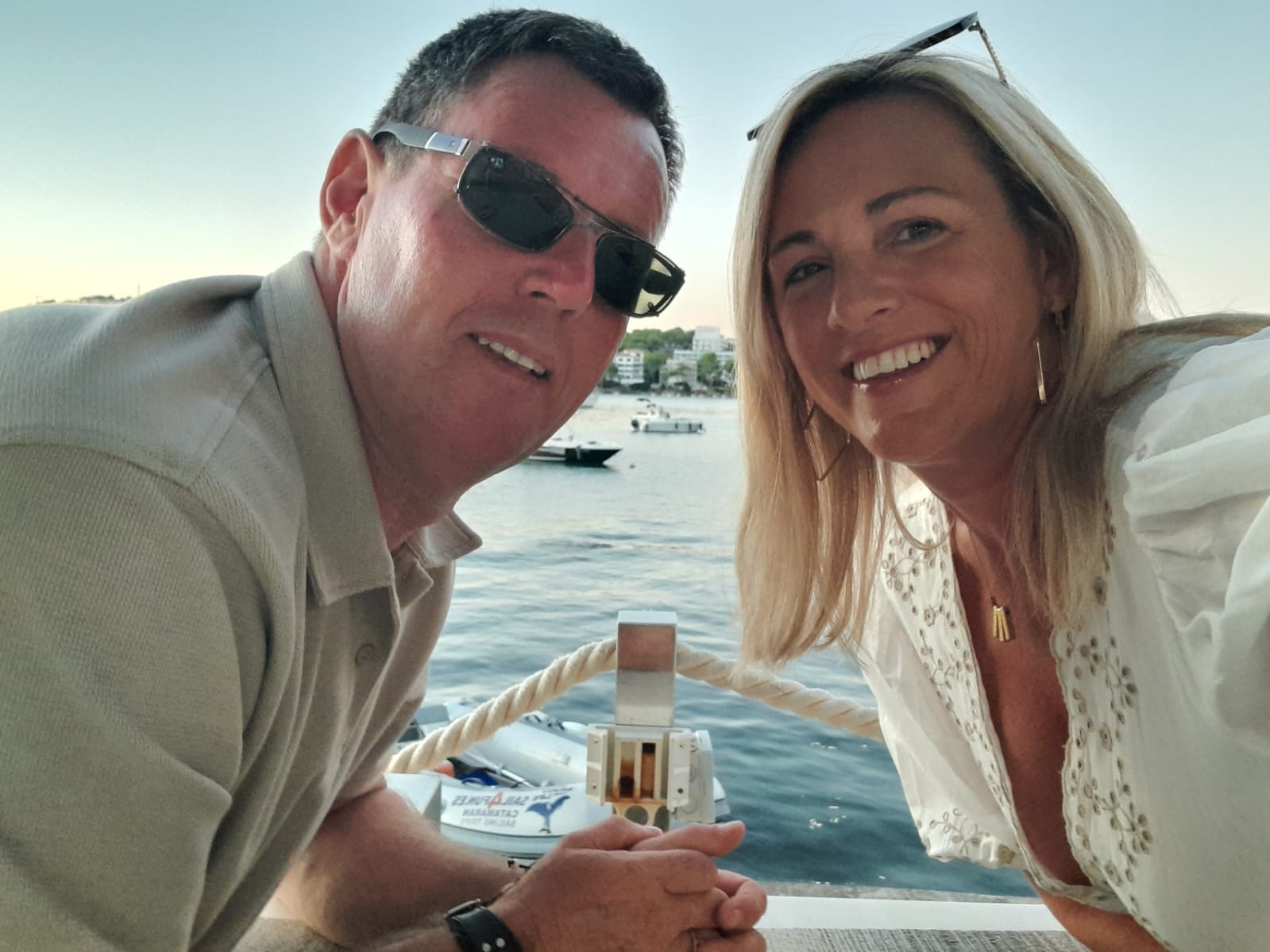 Natalie, wearing glasses on her head, pictured with her husband at a waterside location