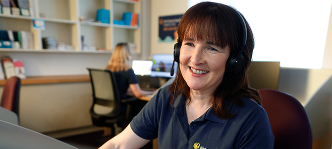 Nurse in navy t-shirt sitting at computer with headset on smiling