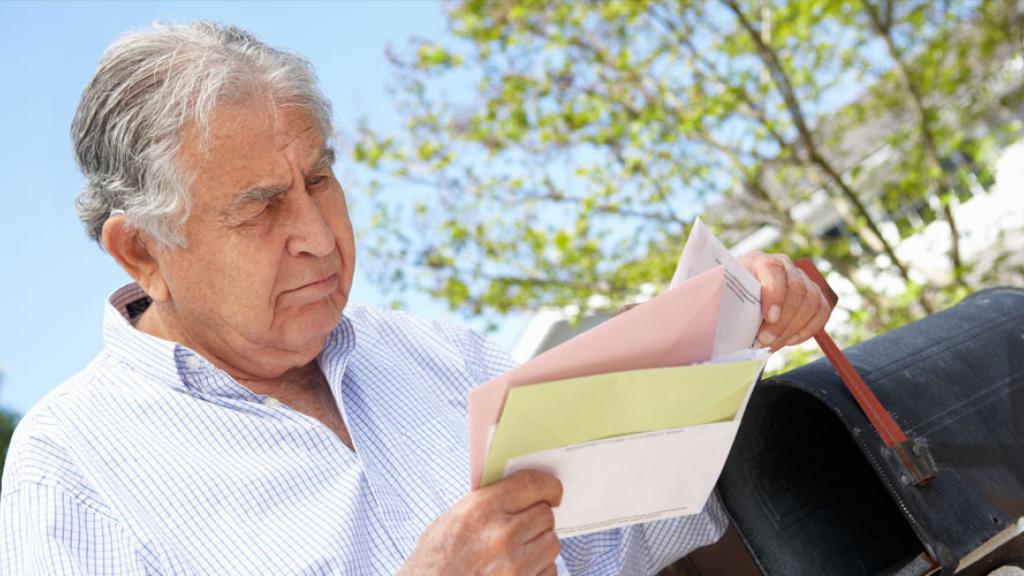 An older man looking at a letter with worry