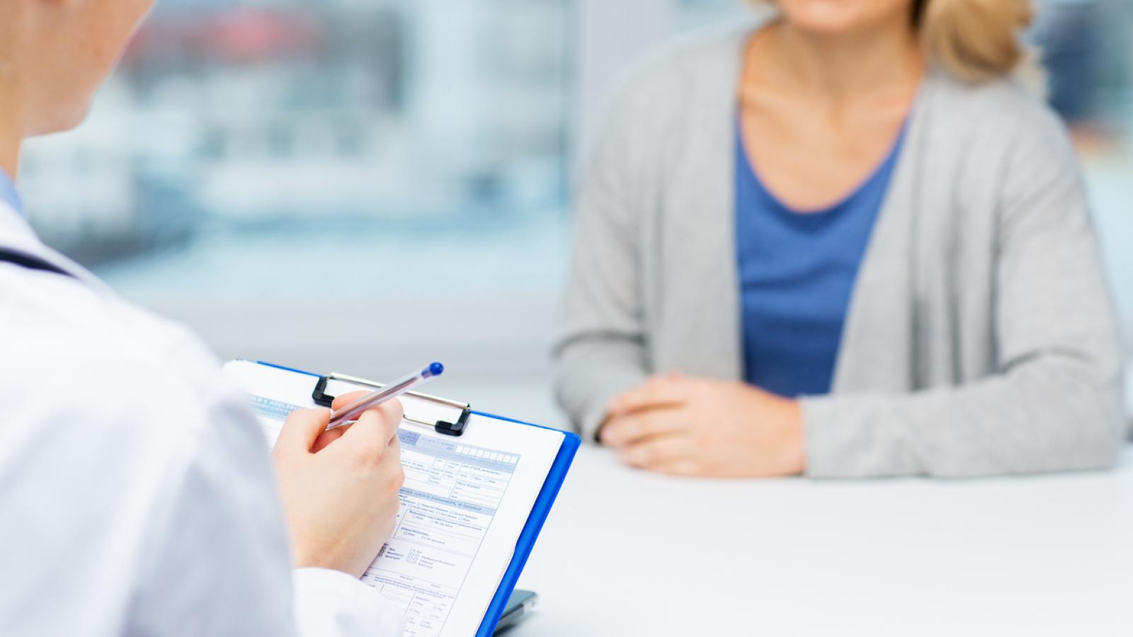 Woman talking to a doctor. The doctor is holding a clipboard.